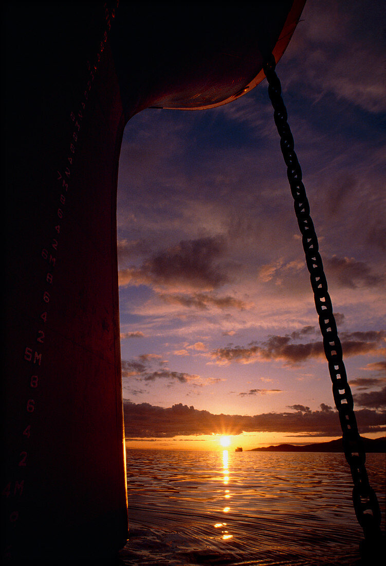 Setting sun framed by bow & anchor line of ship