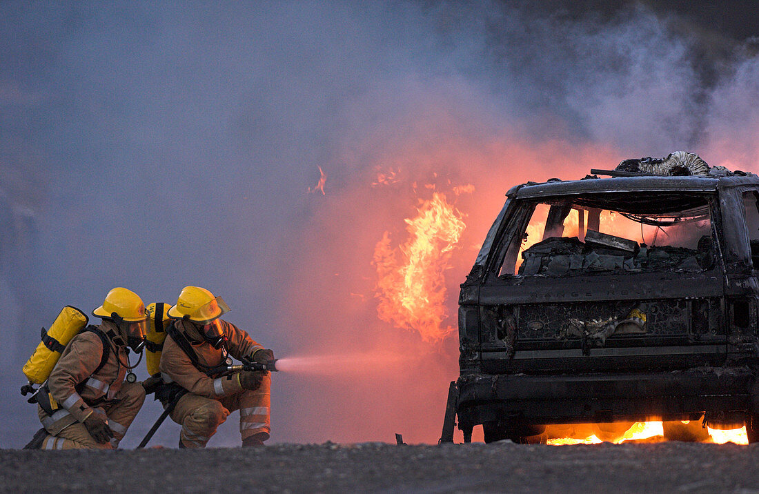 Firefighters hosing a burning car