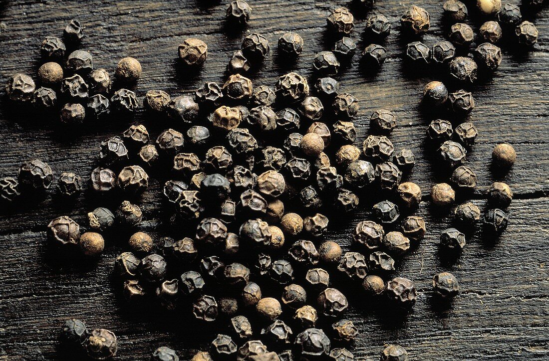 Many Black Peppercorns on Wood Surface