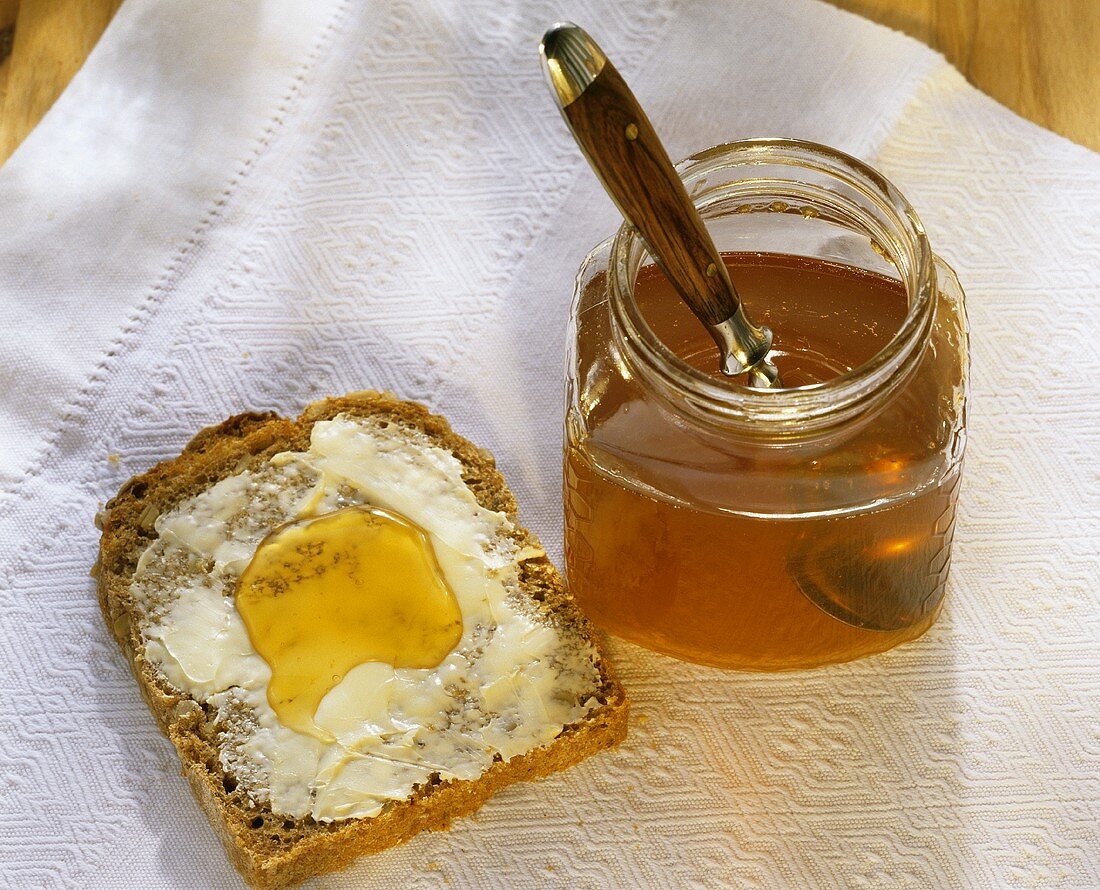 Honig im Glas mit Löffel & Butterbrot mit Honig