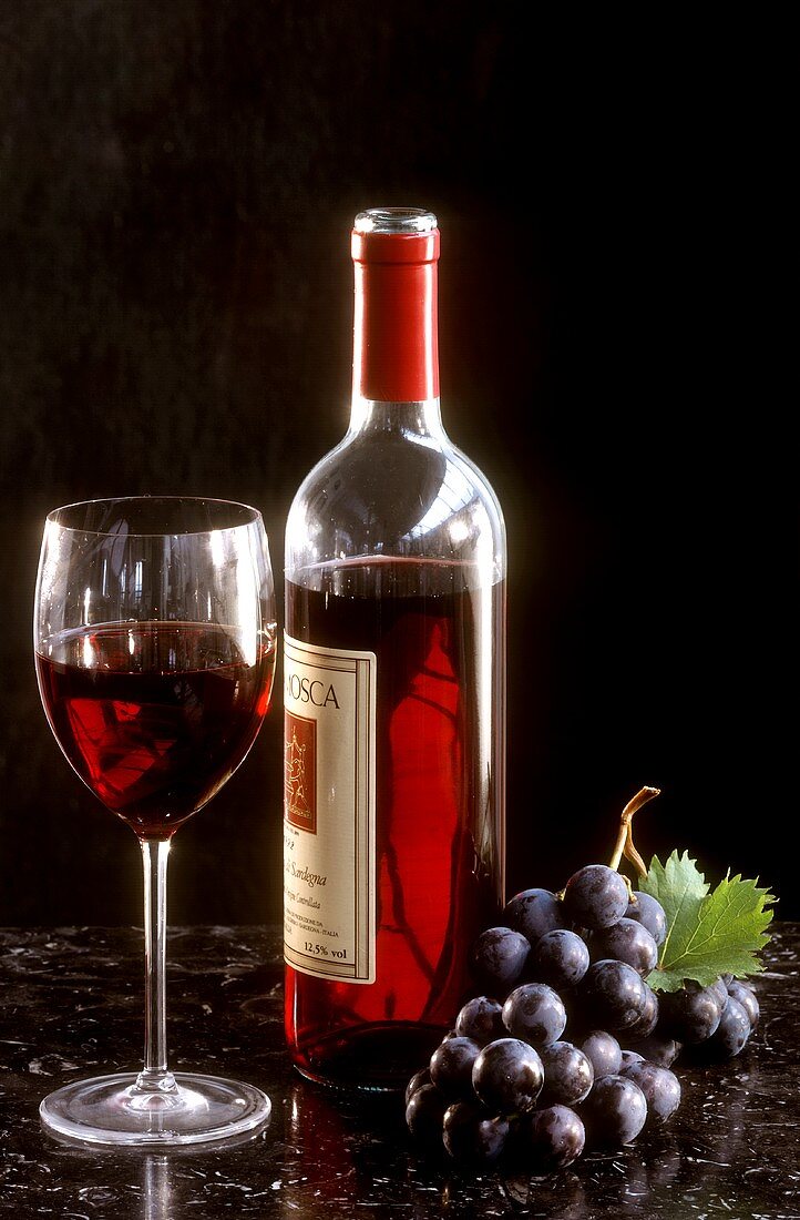 Stillleben mit sardischer Rotweinflasche, Glas und Weintraube