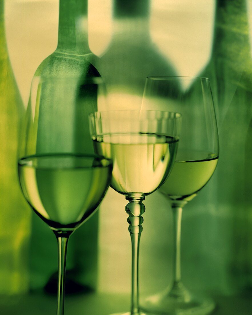 Three white wine glasses in front of bottle silhouette
