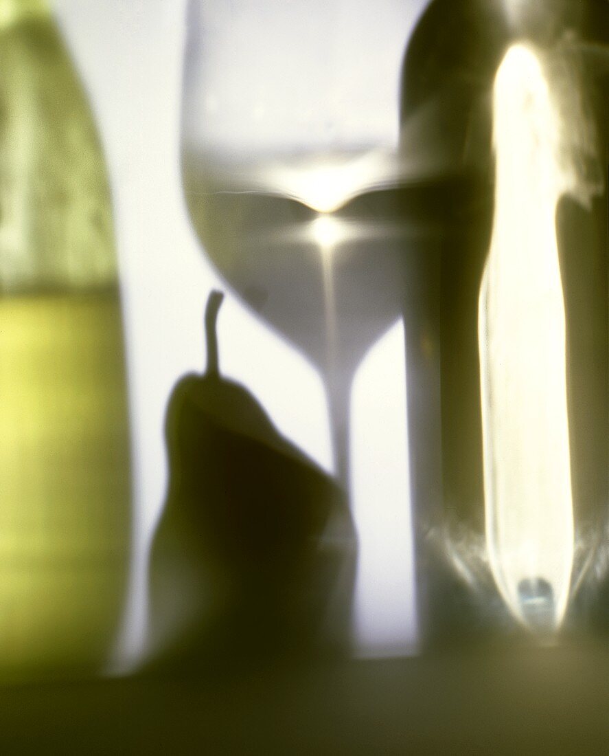 Shadow of a white wine glass, a pear & two bottles