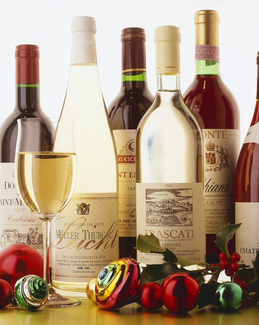 Weißweinglas und Weihnachtskugeln vor diversen Weinflaschen