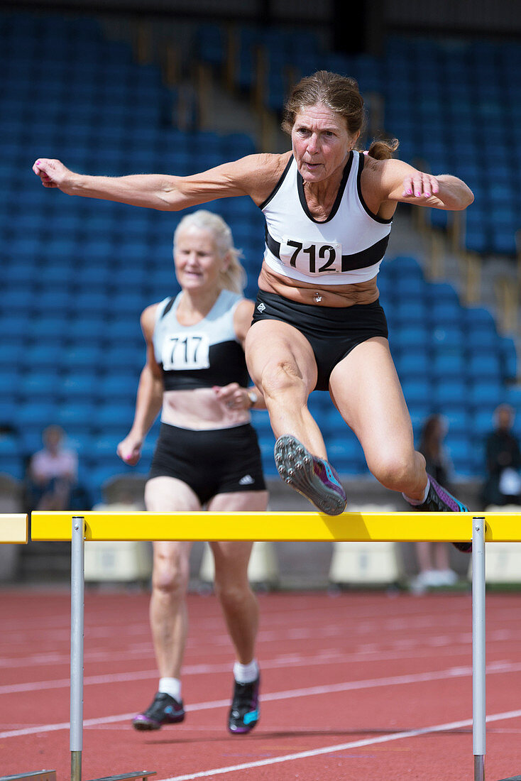 Senior female athlete clears hurdle