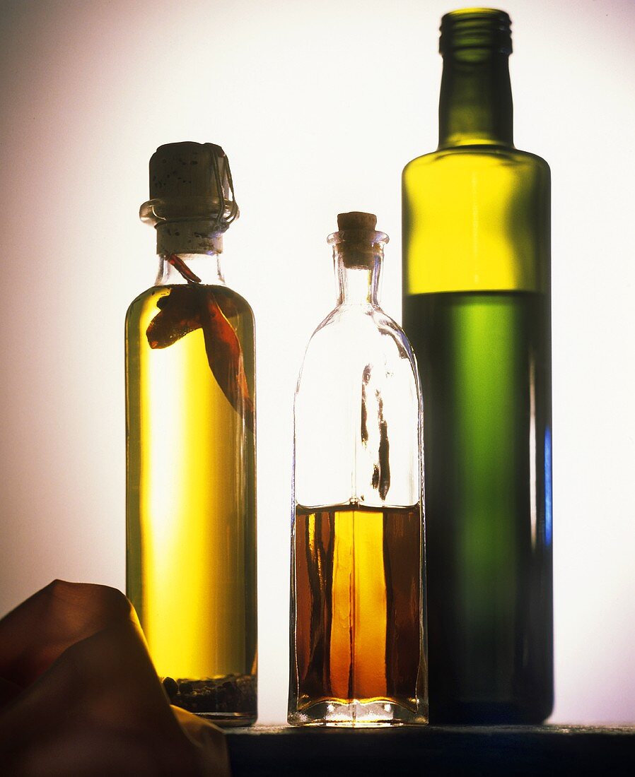 Drei Flaschen mit Olivenöl vor grauem Hintergrund