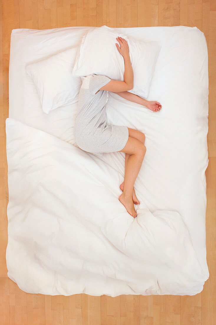 Woman lying in bed with pillow over head