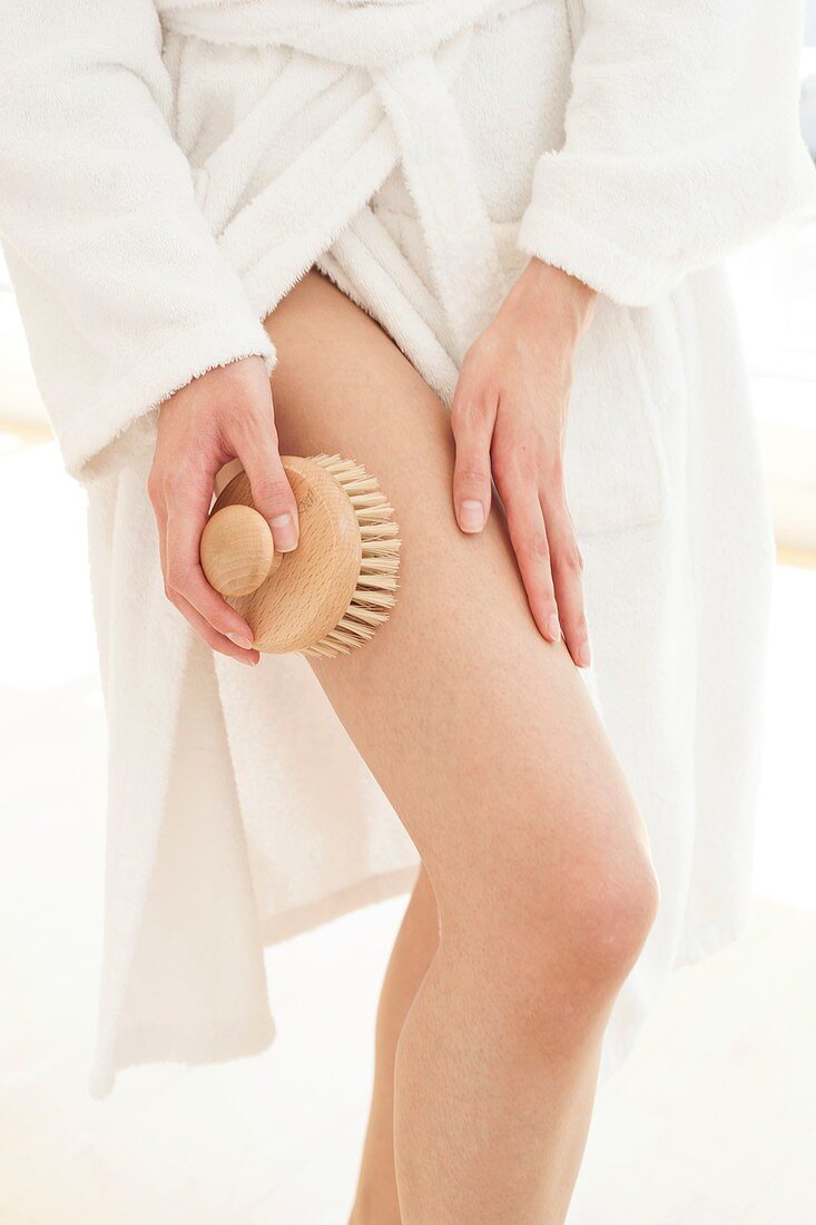 Young woman using body brush on leg