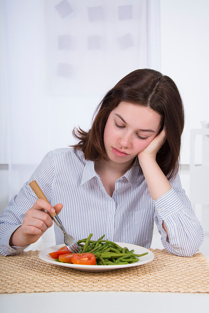 Sad teenage girl with plate of vegetables