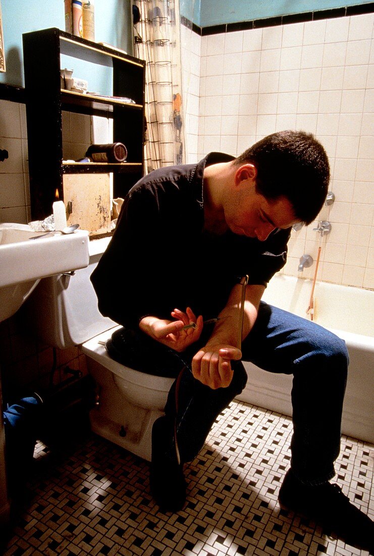 Heroin user injecting arm in bathroom