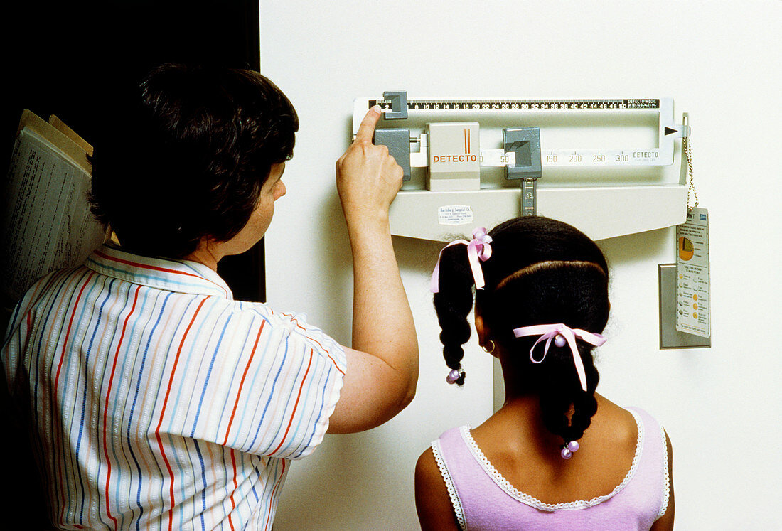 Nurse measures young girl on weighing scales