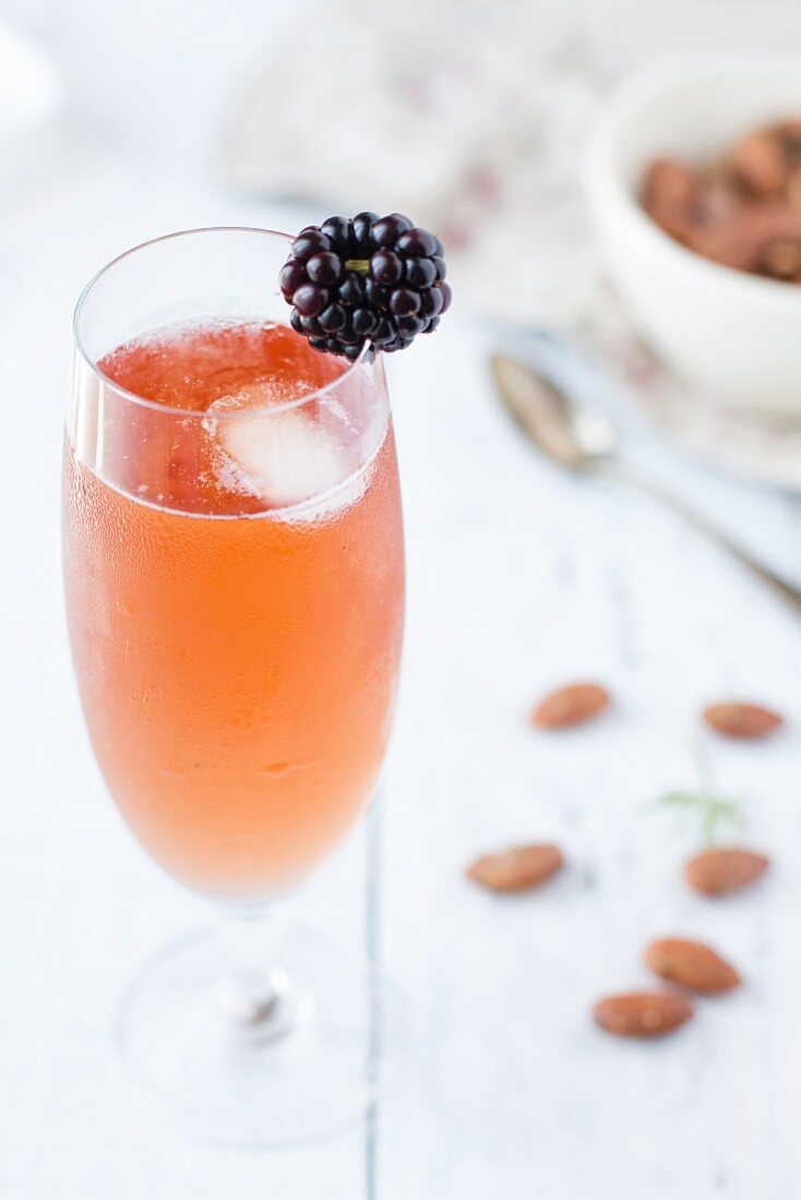 A kir cocktail with a blackberry and an ice cube