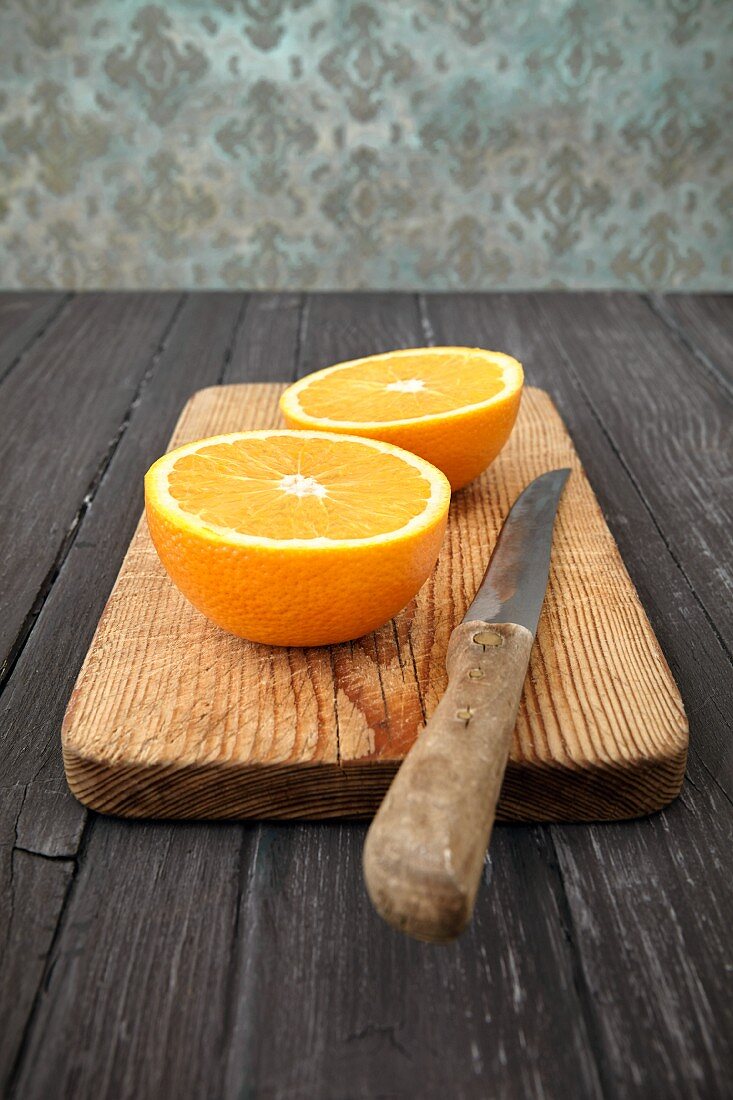 Halbierte Orange mit Messer auf Holzschneidebrett