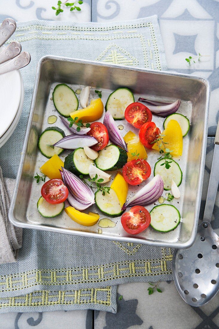 Fresh vegetables in a roasting tin (courgette, onions, tomatoes, yellow pepper, garlic and thyme)