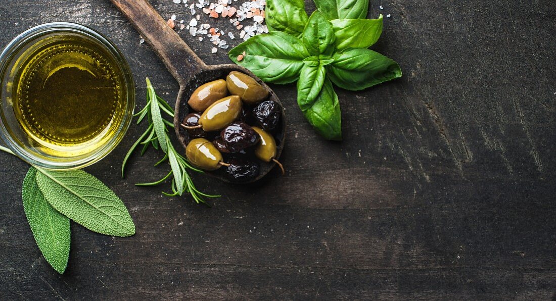 Green and black Mediterranean olives in old cooking spoon with olive oil and herbs