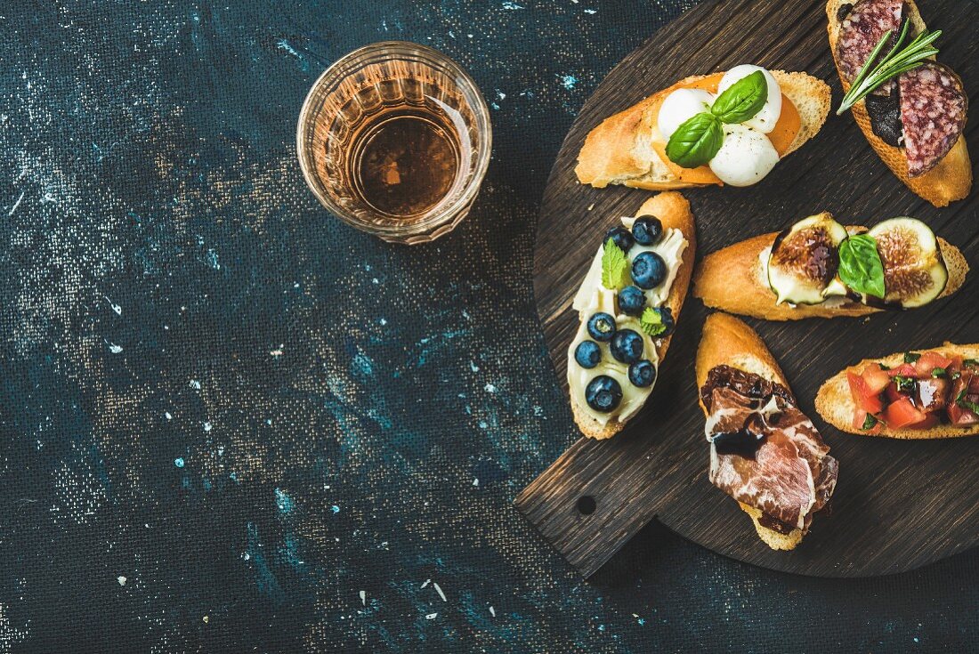 Italian crostini with various toppings on round wooden board and glass of rose wine
