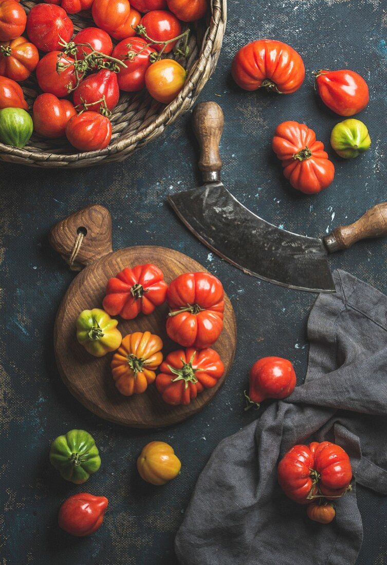 Bunte Heirloom-Tomaten im Korb und Wiegemesser auf schwarzem Untergrund