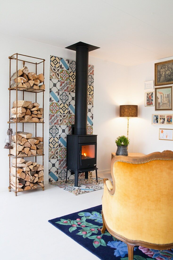 Firewood on shelves next to wood-burning stove on strip of colourful tiles on wall and floor