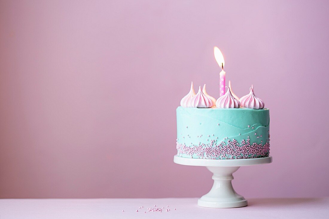 Türkisfarbener Geburtstagskuchen mit einer Kerze vor rosa Hintergrund