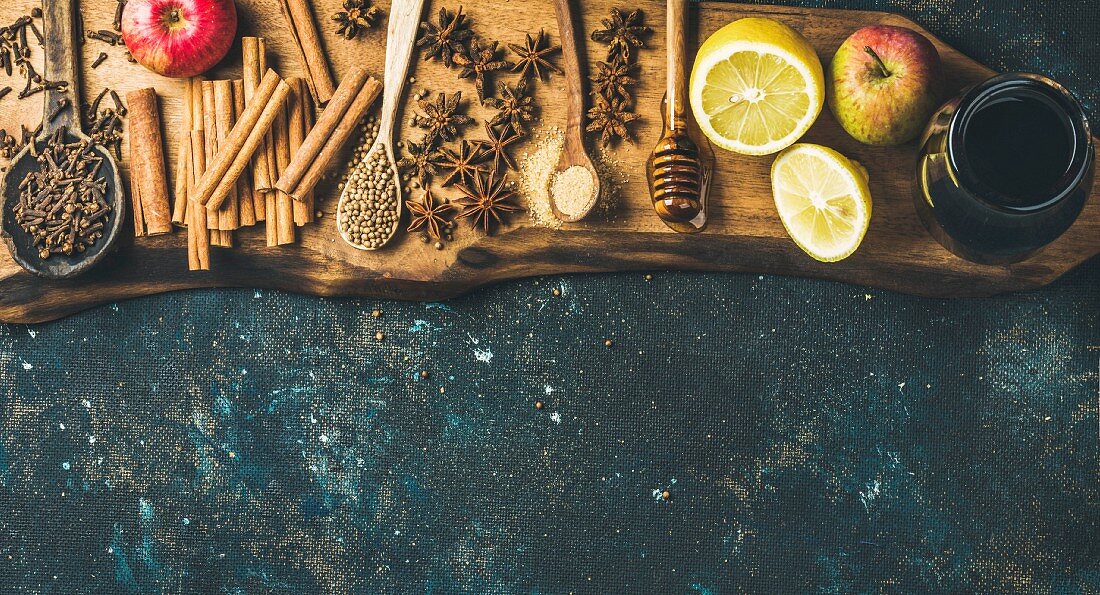 Ingredients for making mulled wine, wine in glass bottle, honey, lemon, apples and spices on wooden board