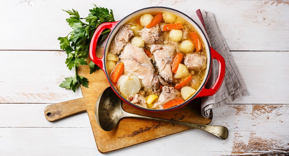 Stewed rabbit with potatoes and carrot in cast iron pot on rustic wooden table background