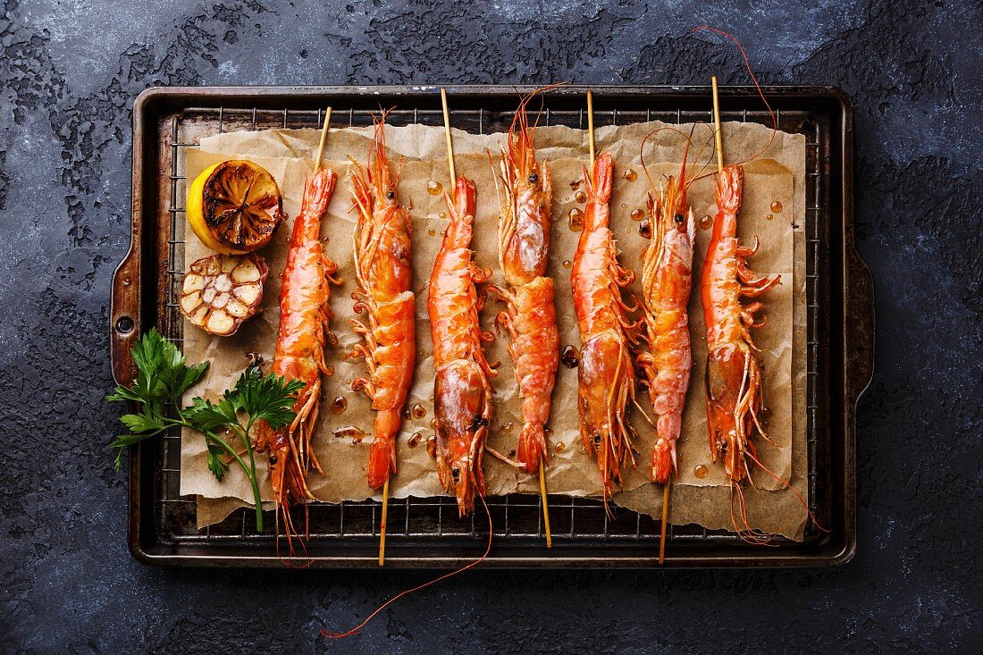 Grilled fried prawns shrimps Langostino Austral on skewers on metal grid baking sheet on black background