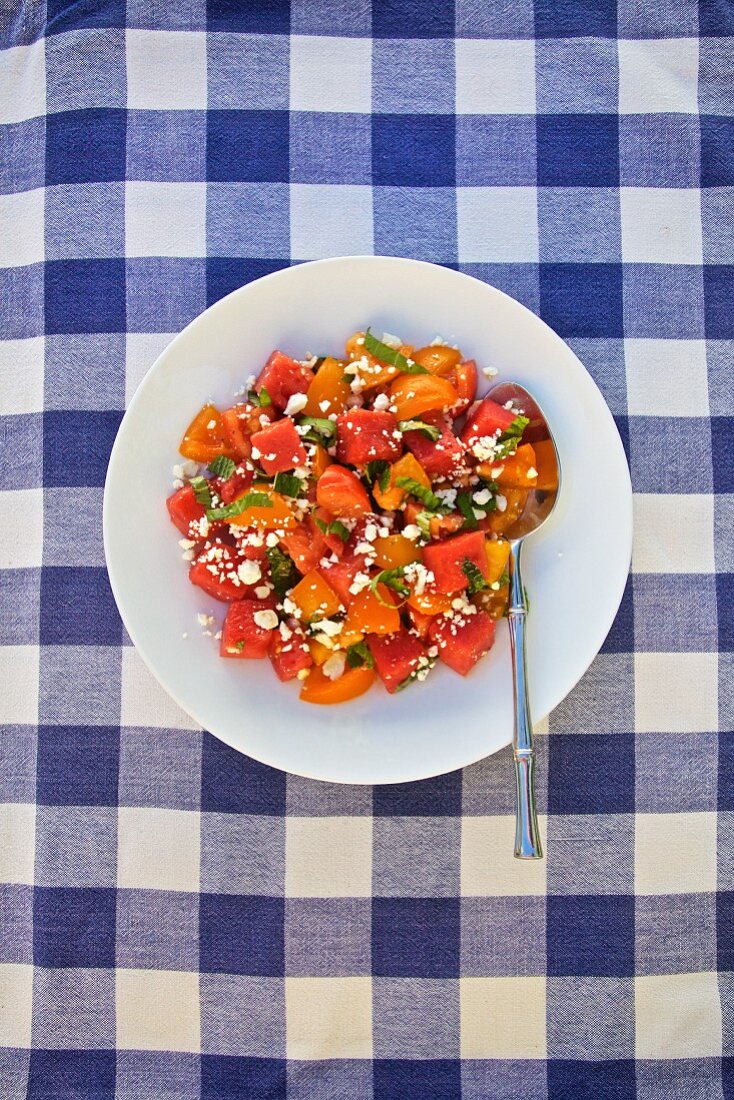 Sommersalat mit Tomaten, Wassermelone, Koriander und Feta auf blau kariertem Tischtuch