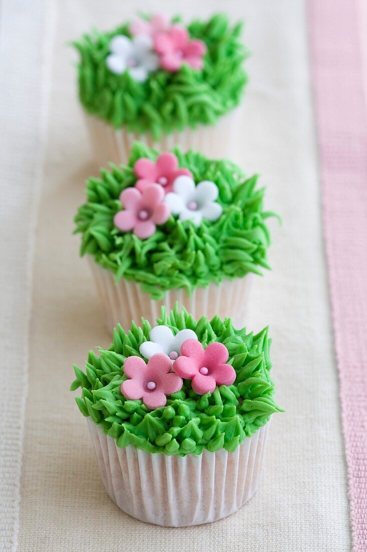 Mini-Cupcakes mit grüner Buttercreem und rosa Zuckerblüten