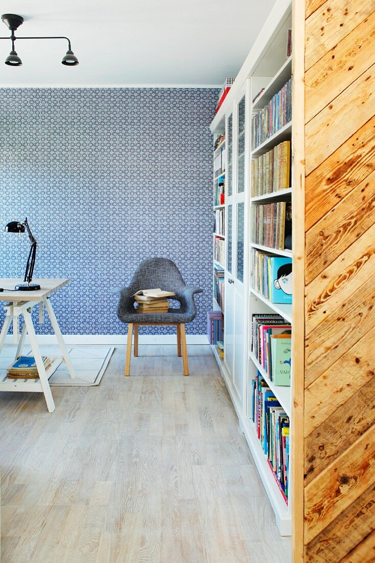 Bücherwand und Armlehnstuhl vor blau-weiß tapezierter Wand