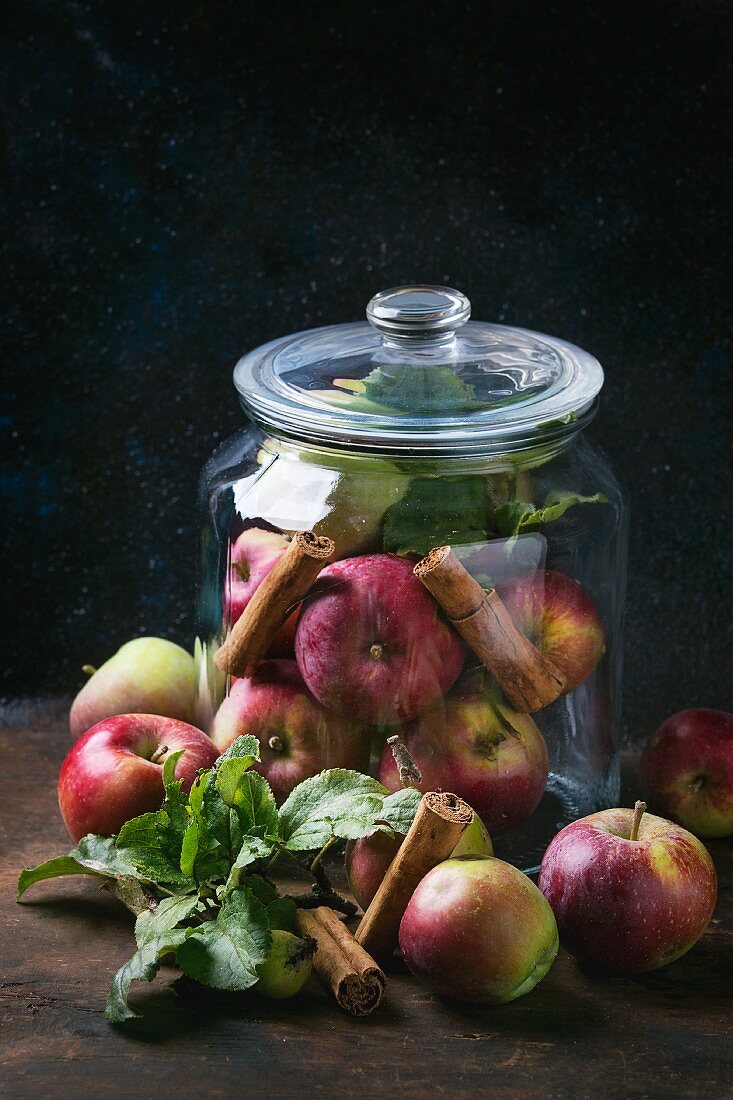 Wildäpfel mit Blättern und Zimtstangen im Vorratsglas