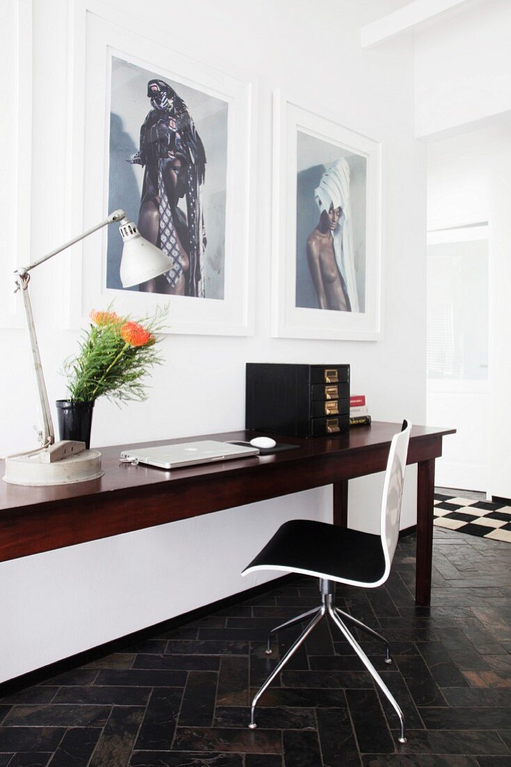 Laptop on exotic-wood table and designer chair below large photos