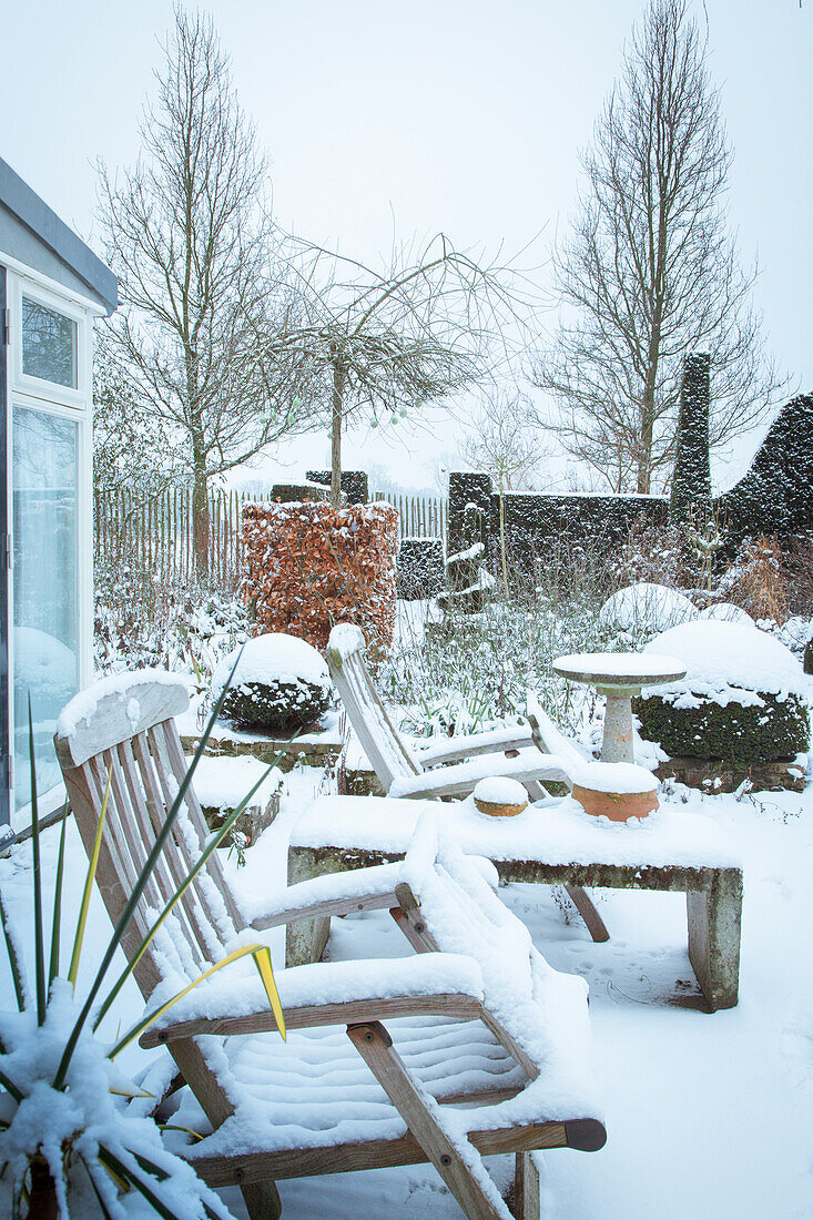 Garden in winter with snow cover and wooden furniture