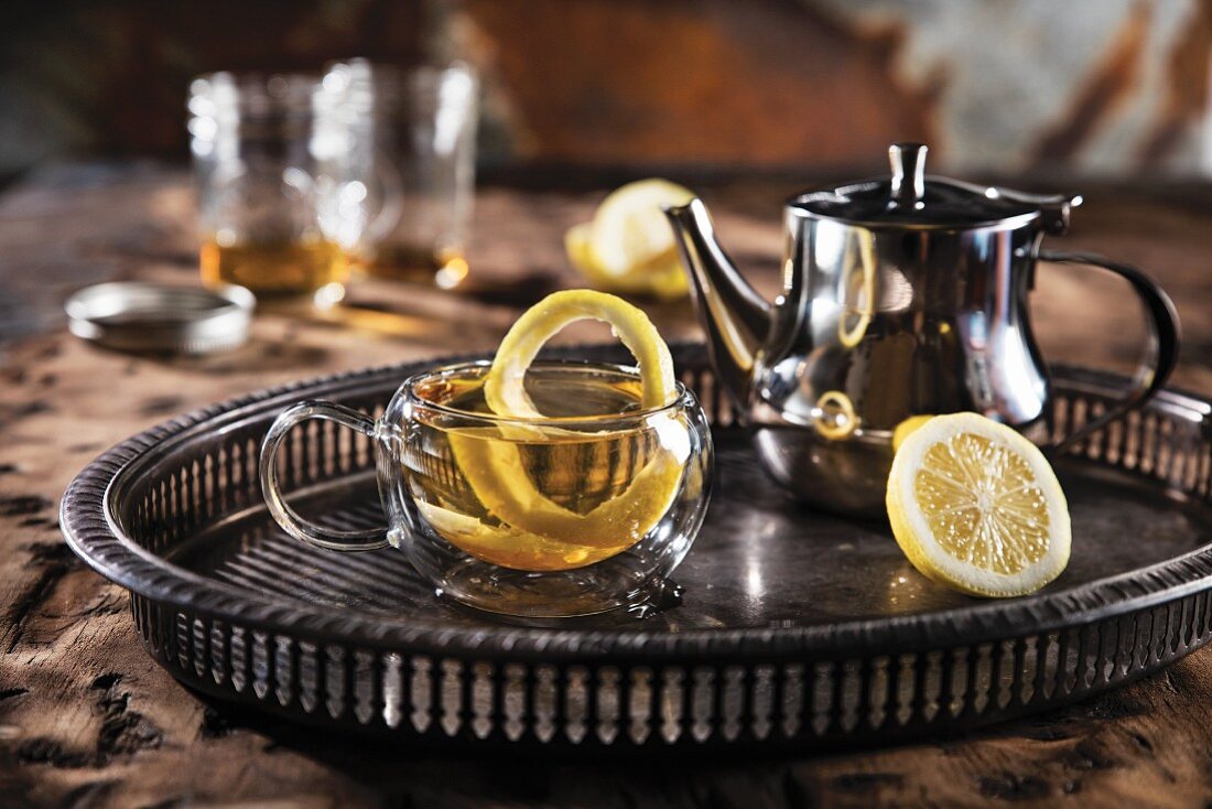 Hot Toddy in Glastasse mit Zitrone und silberner Teekanne
