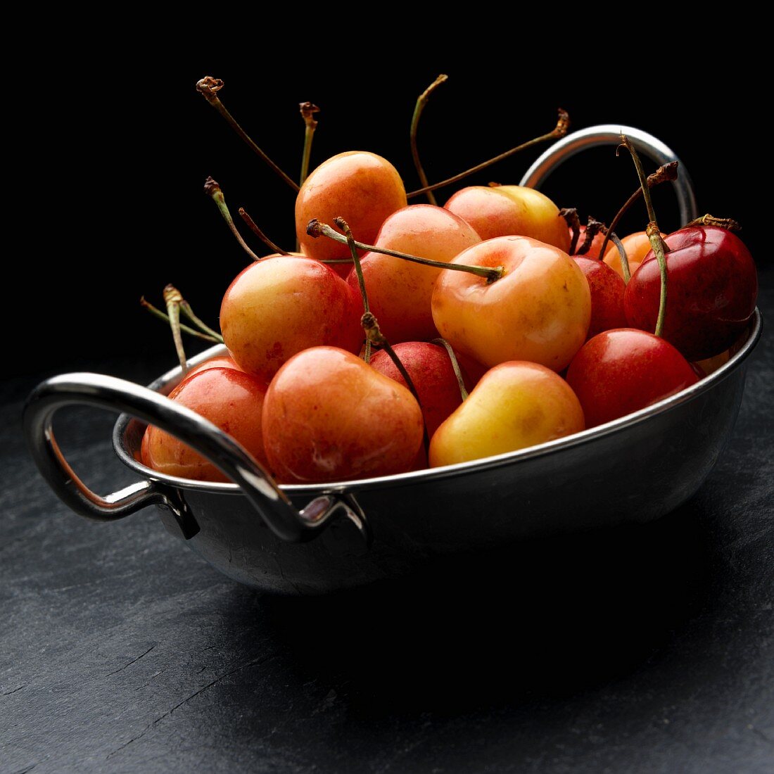Pale red Rainier cherries in a metal bowl