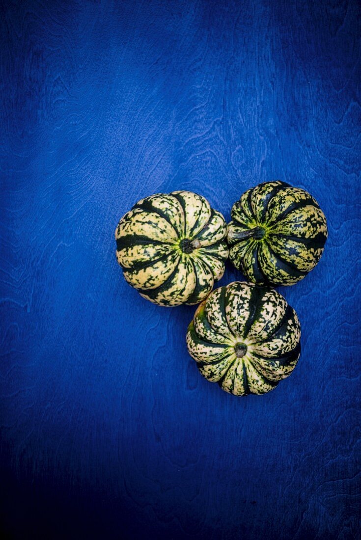 Three green and white pumpkins on a blue surface (seen from above)