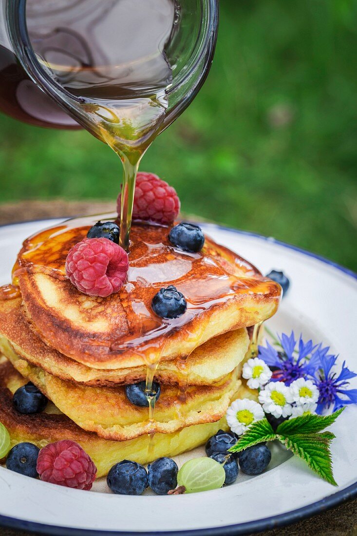 Maple syrup being drizzled on a pile of pancakes with fresh berries