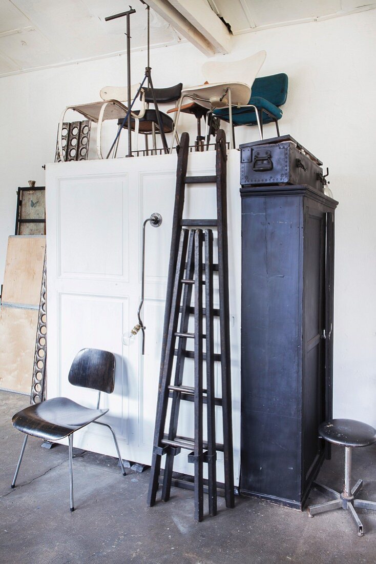 Black ladders and various chairs on white wooden cupboard in tidy workshop