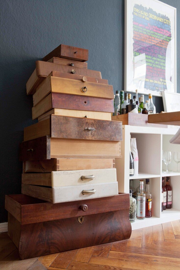 Vintage wooden drawers stacked against dark grey wall next to white open-fronted shelves