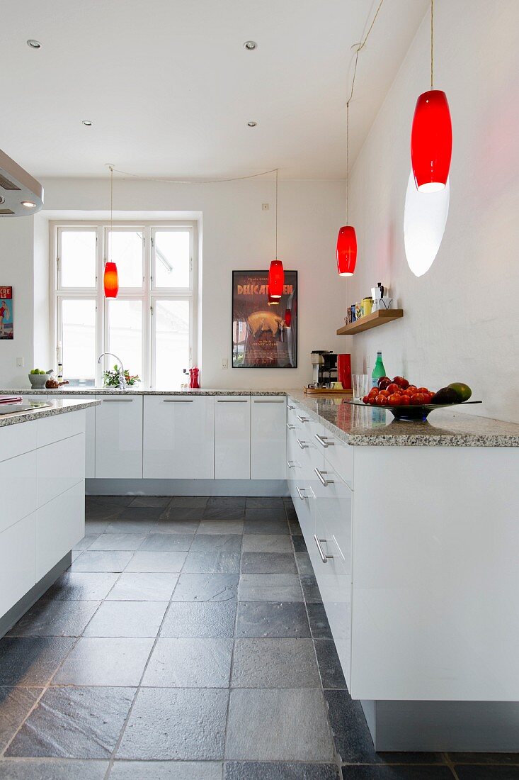 Schlichte, weiße Einbauküche mit Granit-Küchenarbeitsplatte und roten Retro Pendelleuchten