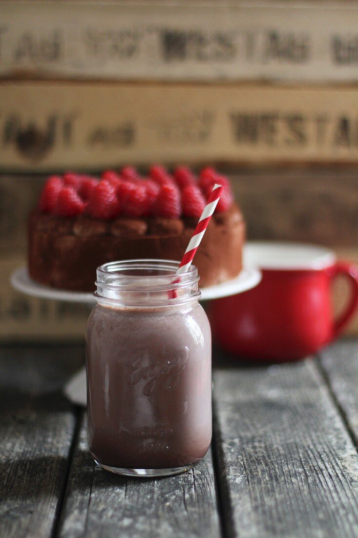 A chocolate milkshake with a straw in a glass jar with raspberry cake in the background