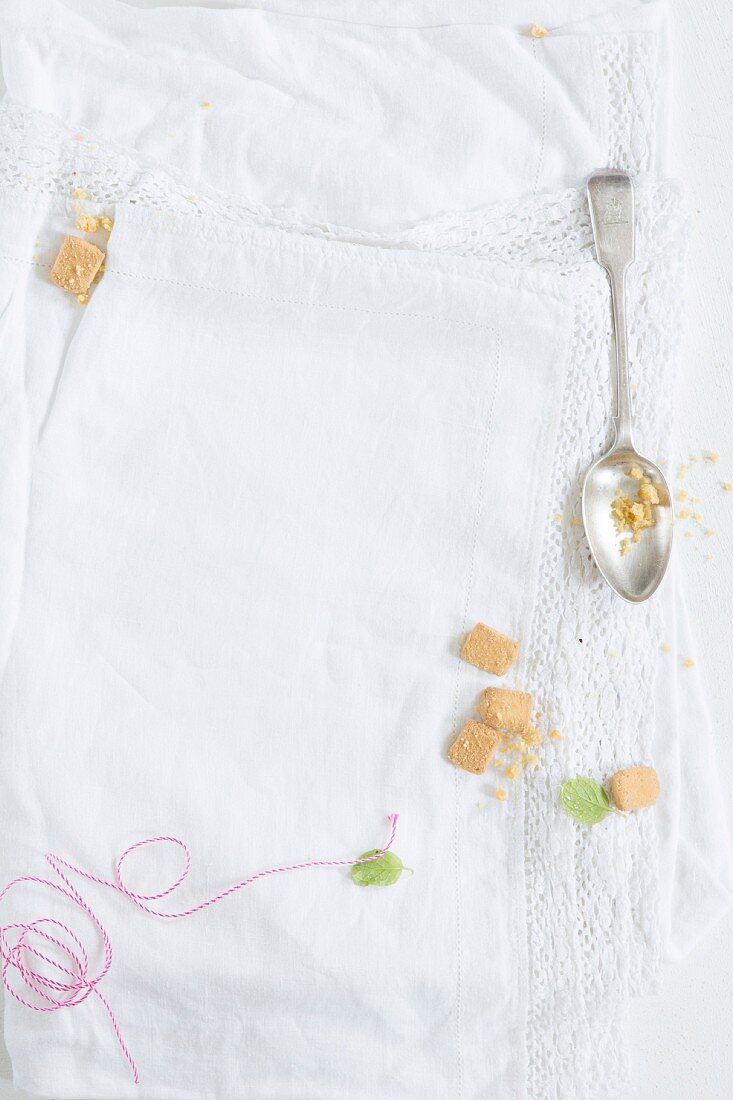 A spoon, biscuit crumbs, and kitchen string on a white tablecloth with a lace border
