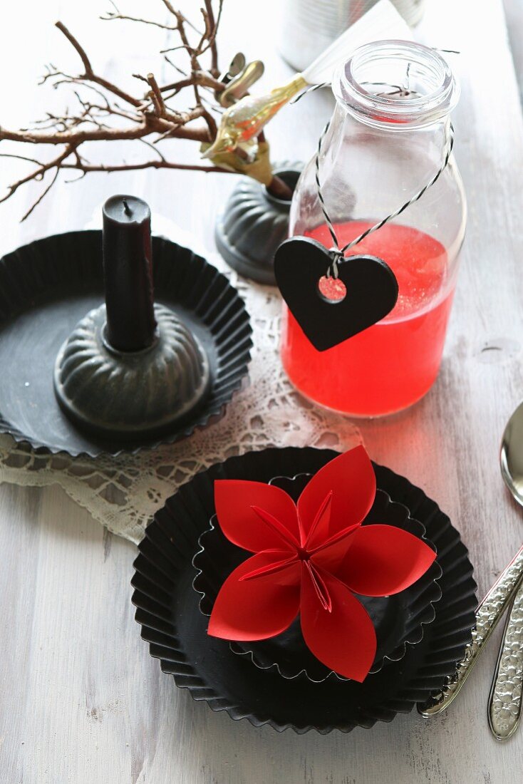 Red origami flower in round tart tin and red drink in bottle