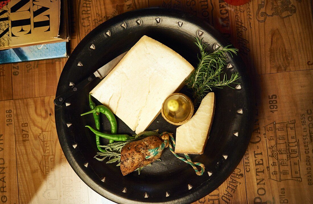 A cheese platter with sausage, rosemary and chilli peppers
