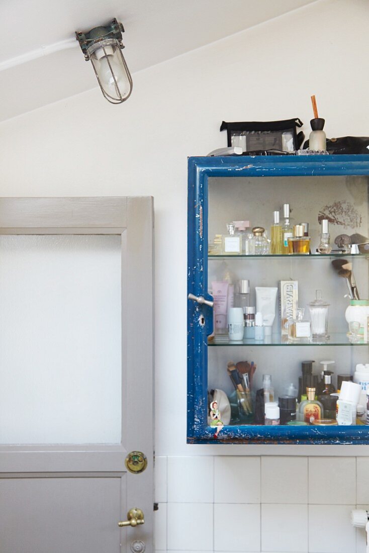 Various perfume bottles and cosmetics in vintage glass-fronted cabinet in bathroom