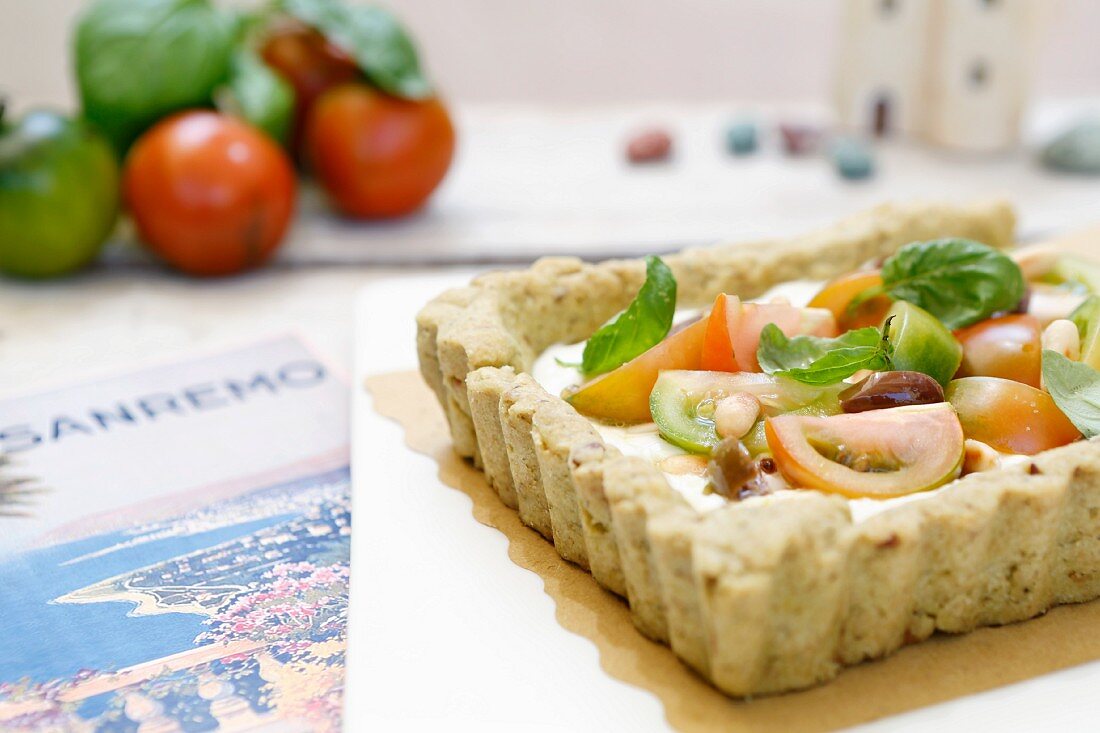 Salty tart with cream cheese, pesto, olives, pine nuts and fresh tomatoes (Liguria, Italy)