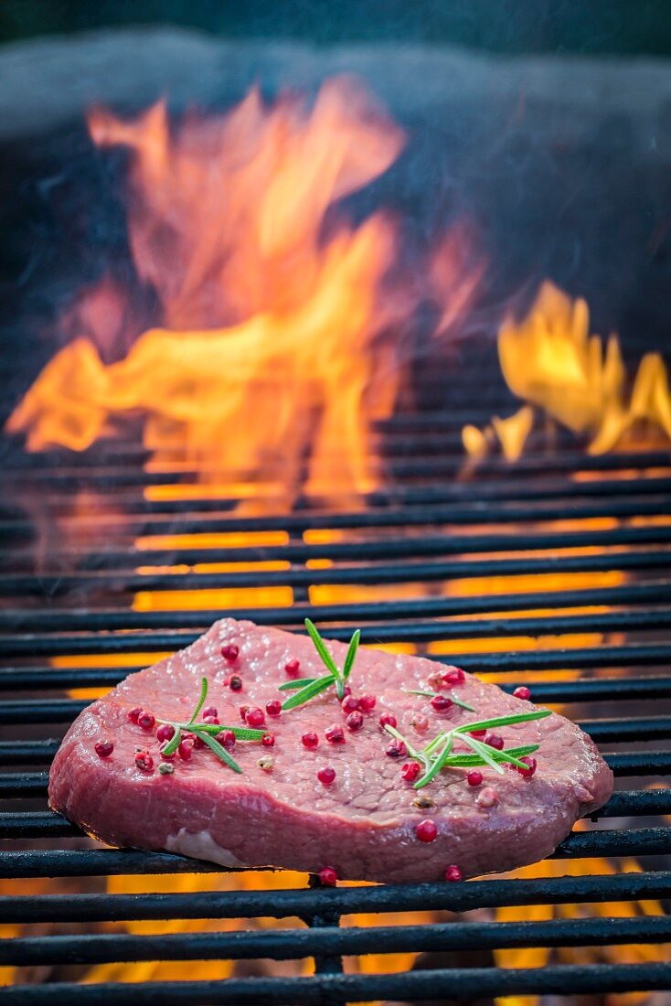 Frisches Steak mit Pfeffer und Rosmarin auf Grillrost mit Feuer