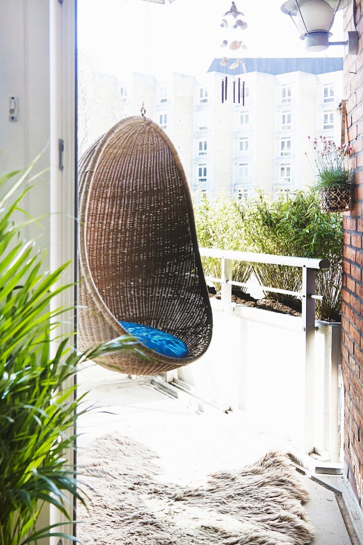 Gemütlicher Korb-Hängesessel auf sommerlichem Balkon