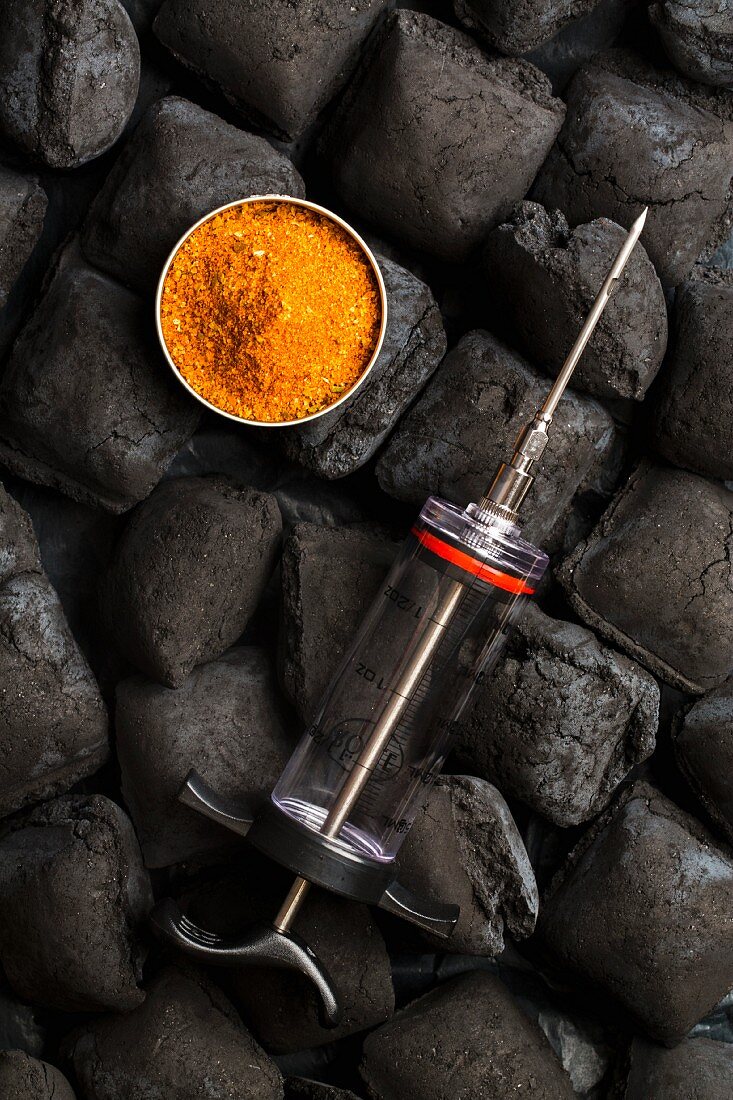 Utensils for barbecued pulled pork: charcoal made of coconut shells, rub and a marinade injector