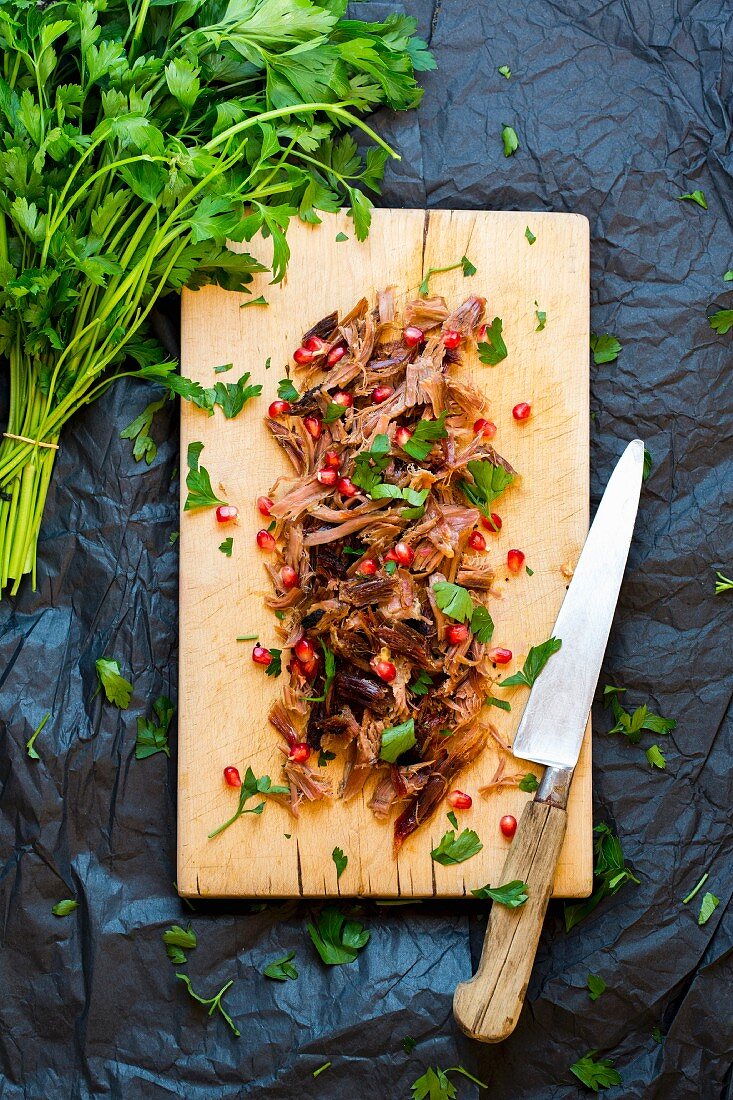 Pulled pork with parsley and pomegranate seeds on a wooden board