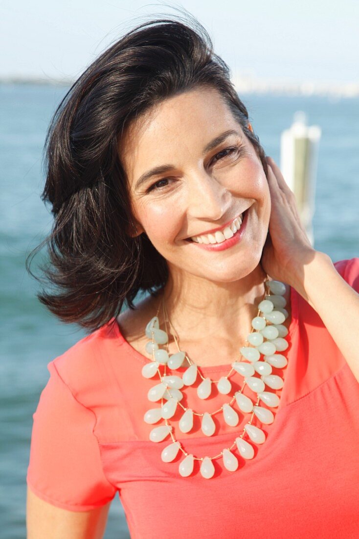 A brunette woman wearing an airy red shirt and a statement necklace
